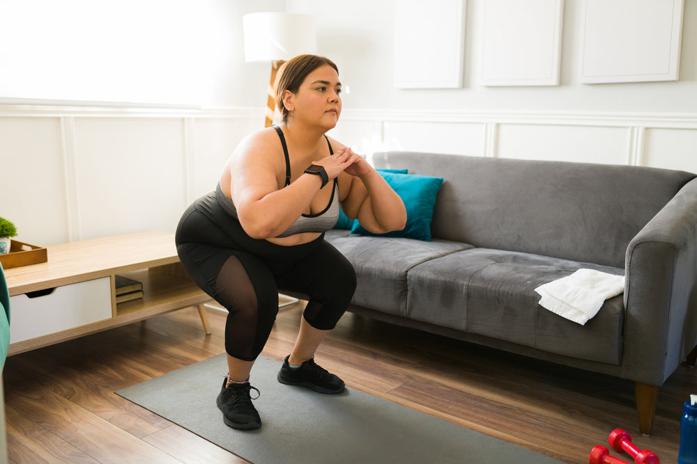 Une femme en tenue d’entraînement qui fait un squat sur un tapis d’exercice dans un salon